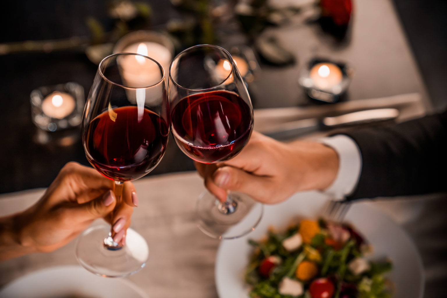 close-up-of-young-couple-toasting-with-glasses-of-red-wine-at